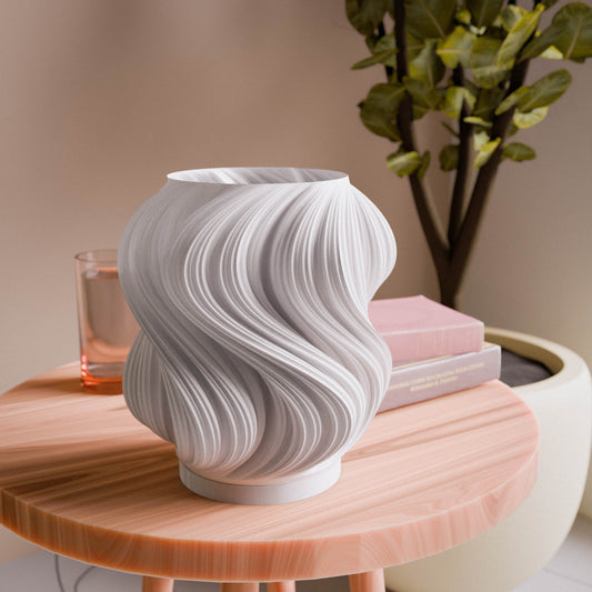 White textured vase on a wooden table with a plant and books in the background
