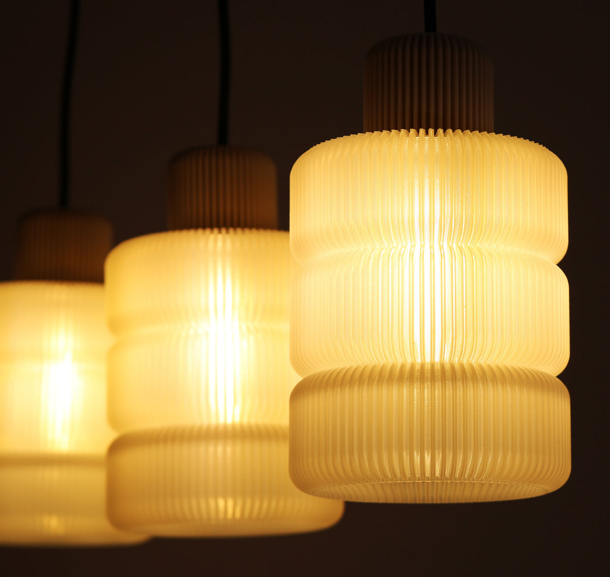 Three illuminated pendant lights with ribbed glass shades on a dark background