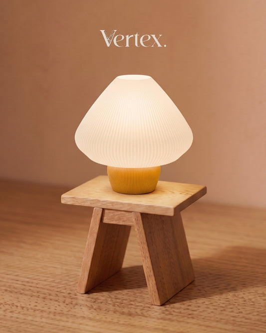 Table lamp with ribbed white shade and yellow base on a  stool against a beige background, featuring the brand 'Vertex'.