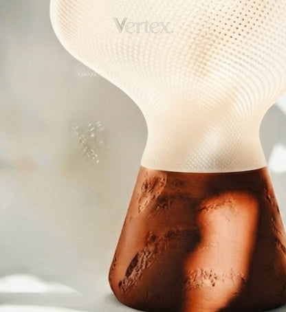 A close-up of a modern table lamp with a textured white upper shade and a sculptural, cratered brown base, featuring the Vertex brand name.
