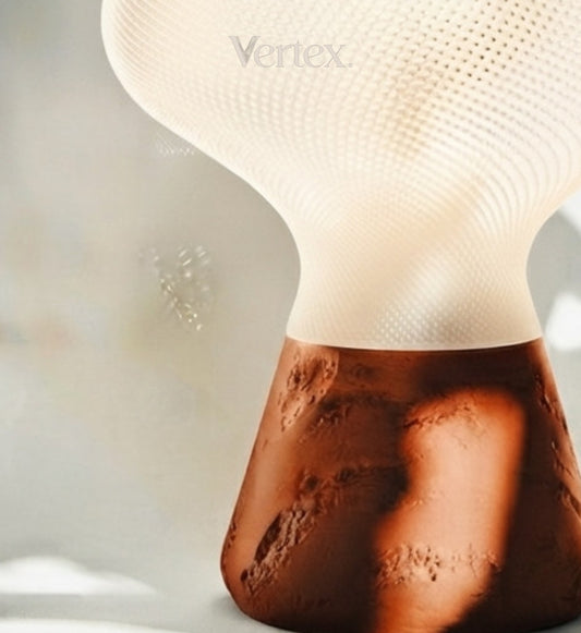 A close-up of a modern table lamp with a textured white upper shade and a sculptural, cratered brown base, featuring the Vertex brand name.