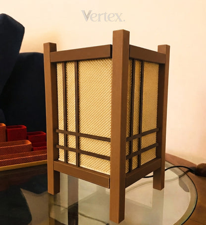 A square wooden table lamp with a warm brown frame and beige woven paper panels, shown on a glass table in an indoor setting.
