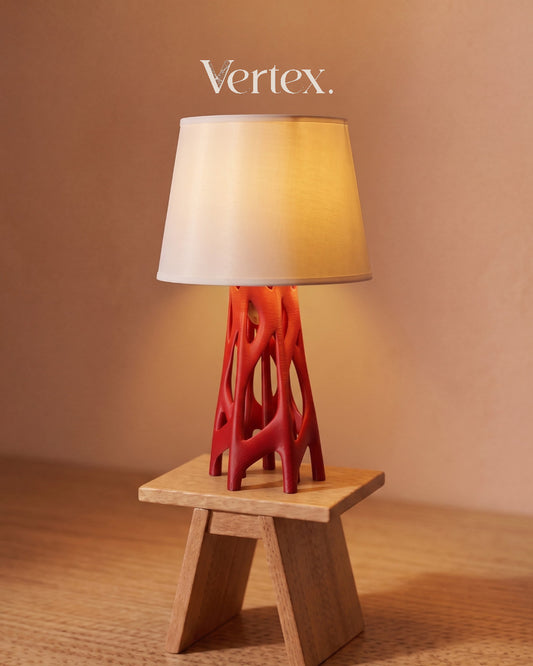 Table lamp with red base and white shade on a wooden stool against a beige wall, featuring the brand 'Vertex'.